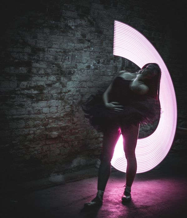Woman in a peaceful yoga pose against a dark background with pink neon highlights.